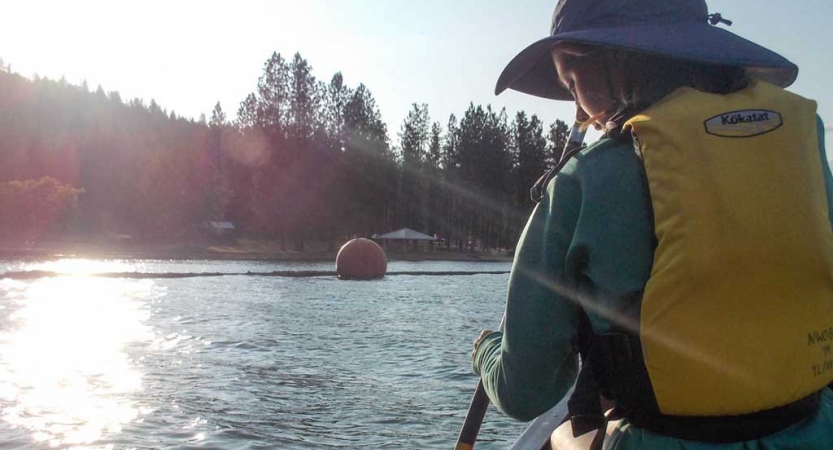 a girl wearing a yellow life jacket paddles a canoe